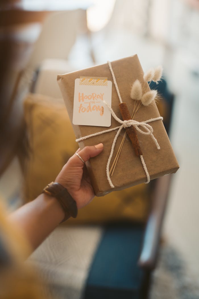 Home Close-up of a beautifully wrapped gift box with rustic twine and dried flowers in hand, creating a warm and inviting atmosphere.